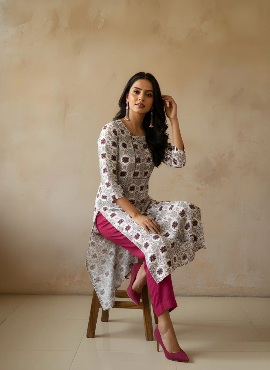 Woman sitting on a stool wearing a patterned kurta with a pink skirt against a beige background